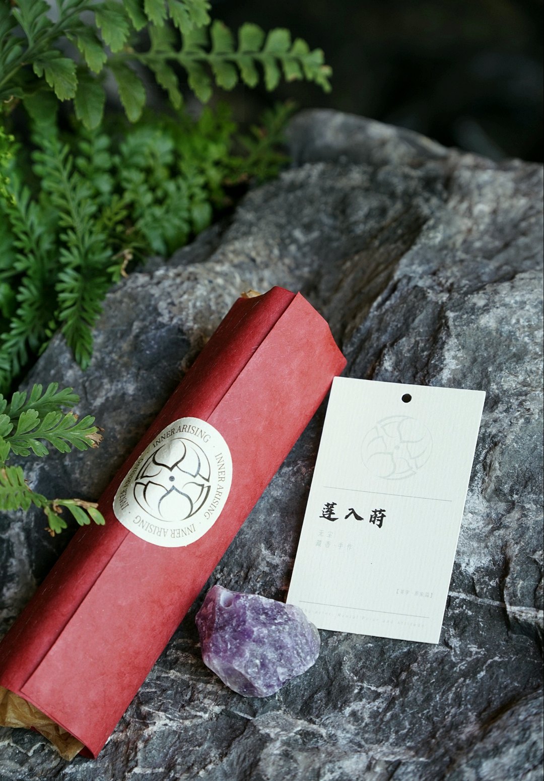 红色纸卷藏香与印着「莲入莳」的白色吊牌,并排放在深色岩石上